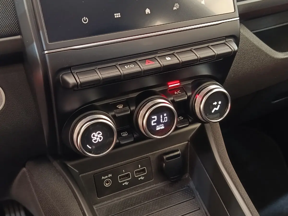 Gros plan sur la console centrale noire de la Renault ZOE blanche, avec commandes de climatisation numériques et ports USB visibles.