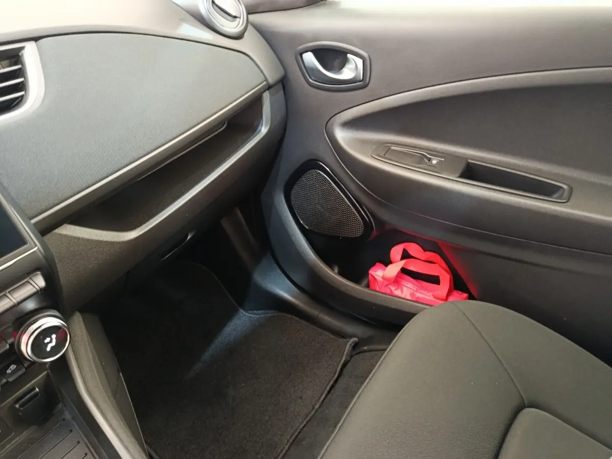 Intérieur côté passager avant de la Renault ZOE blanche, avec porte noire et sac rose dans le rangement.