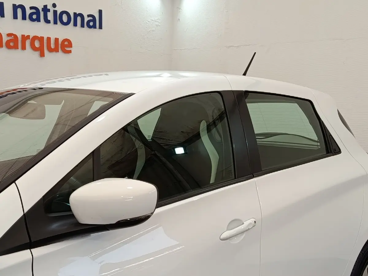 Vue latérale droite d'une Renault ZOE Business blanche, avec rétroviseur et poignées assortis, intérieur partiellement visible.