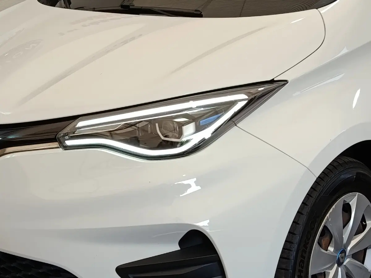 Gros plan sur le phare avant droit blanc de la Renault ZOE 2021 avec jante alu et carrosserie lisse.