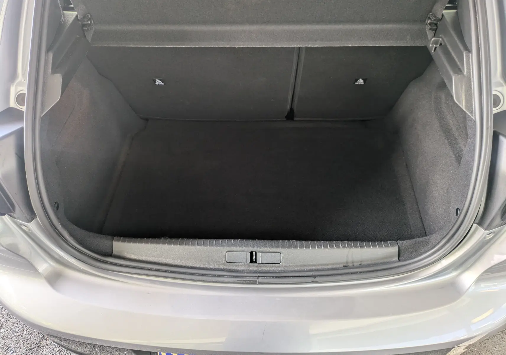 Coffre ouvert de la Peugeot 208 Hybrid 145 gris artense, vue arrière montrant l'espace de chargement vide.