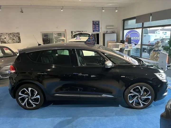 Profil côté gauche d'un Renault Scénic IV noir étoile métal avec toit gris, présenté en showroom lumineux.