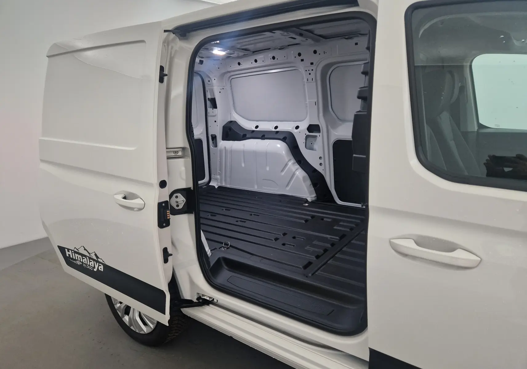 Vue latérale gauche du Volkswagen Caddy Maxi blanc avec porte coulissante ouverte montrant l'espace de chargement vide et le logo Himalaya.