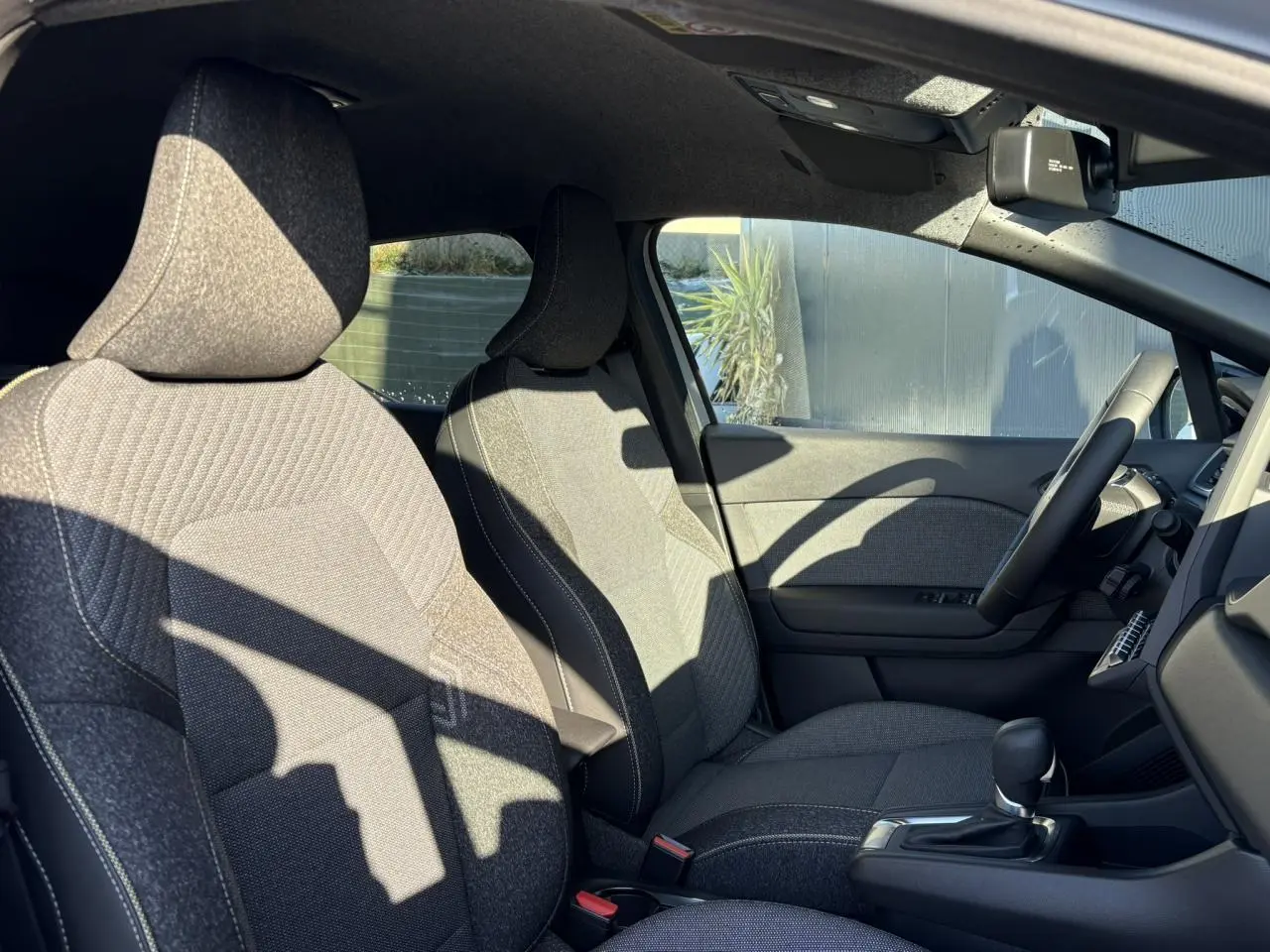 Vue intérieure côté conducteur du Renault Captur 2025, sièges tissu gris avec console centrale et volant textile.