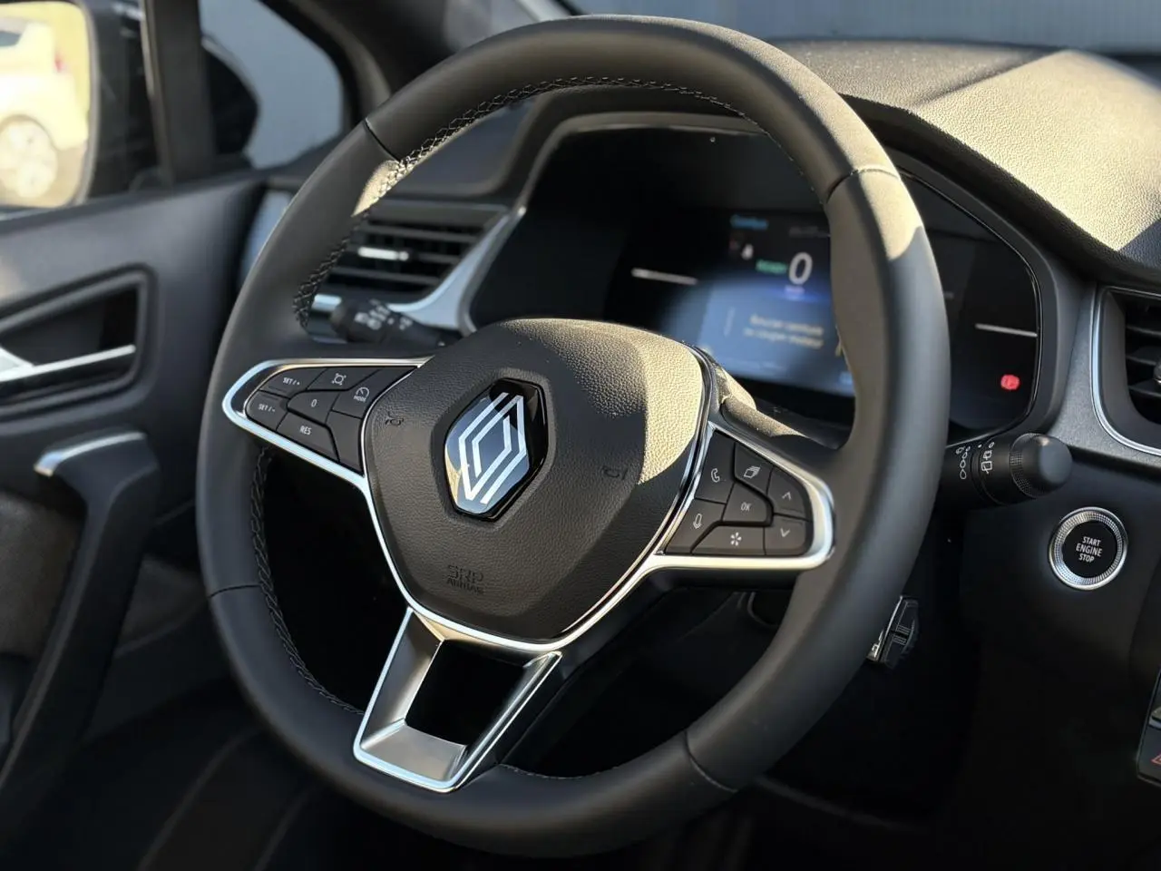 Vue rapprochée du volant noir avec logo Renault et tableau de bord numérique du Captur gris Rafale 2025.