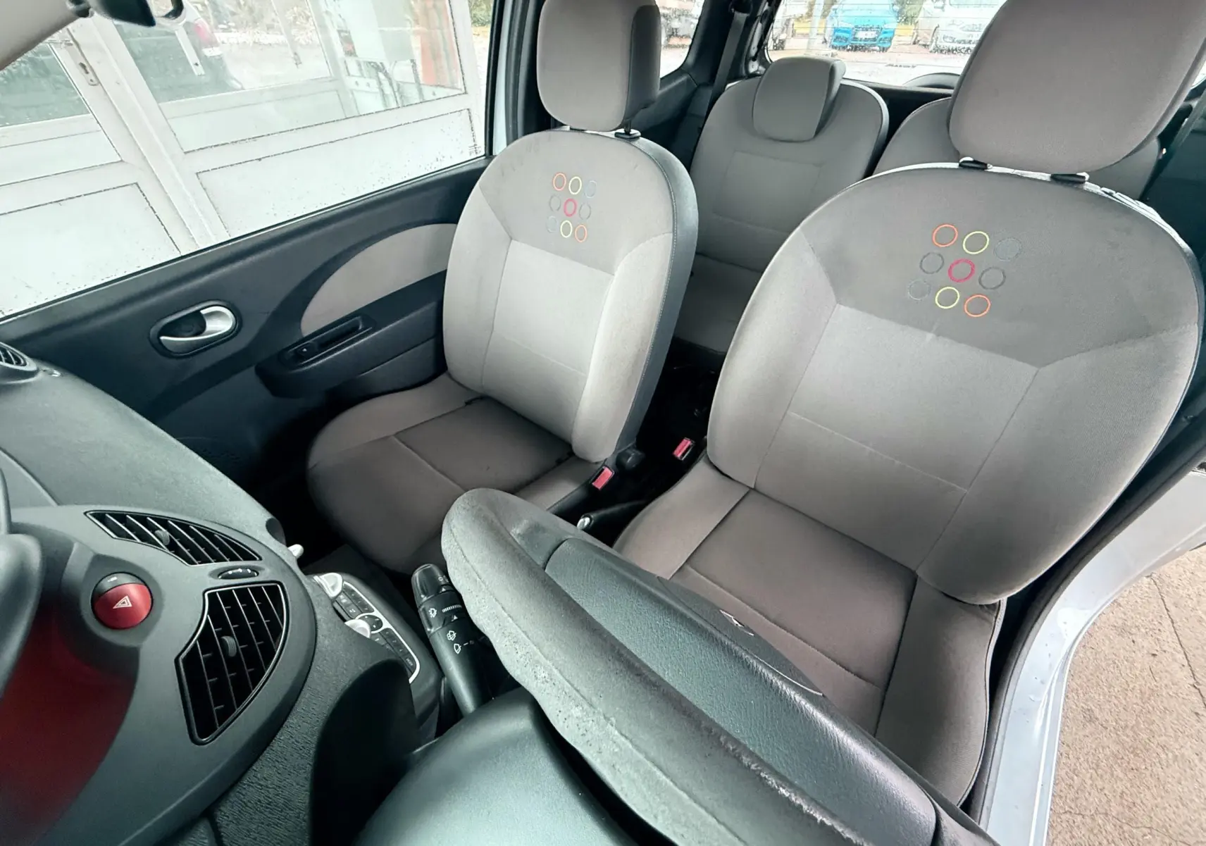 Vue intérieure avant droite de la Renault Twingo II 2009, sièges gris avec motifs colorés et volant cuir visible.
