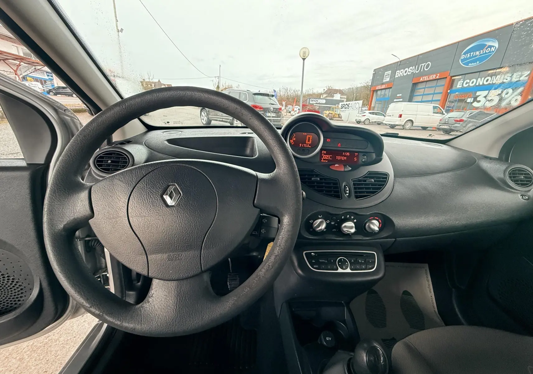 Vue intérieure du tableau de bord et volant noir de la Renault Twingo II gris, avec commandes et affichage digital.