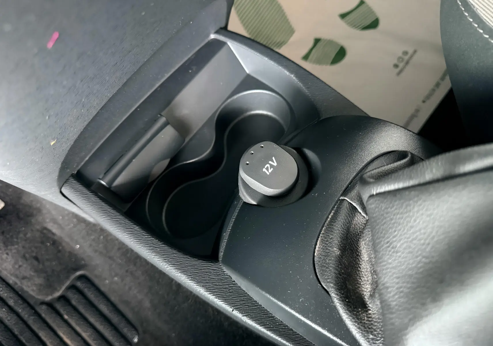 Gros plan sur la console centrale noire de la Renault Twingo II, avec prise 12V et frein à main en cuir visible.