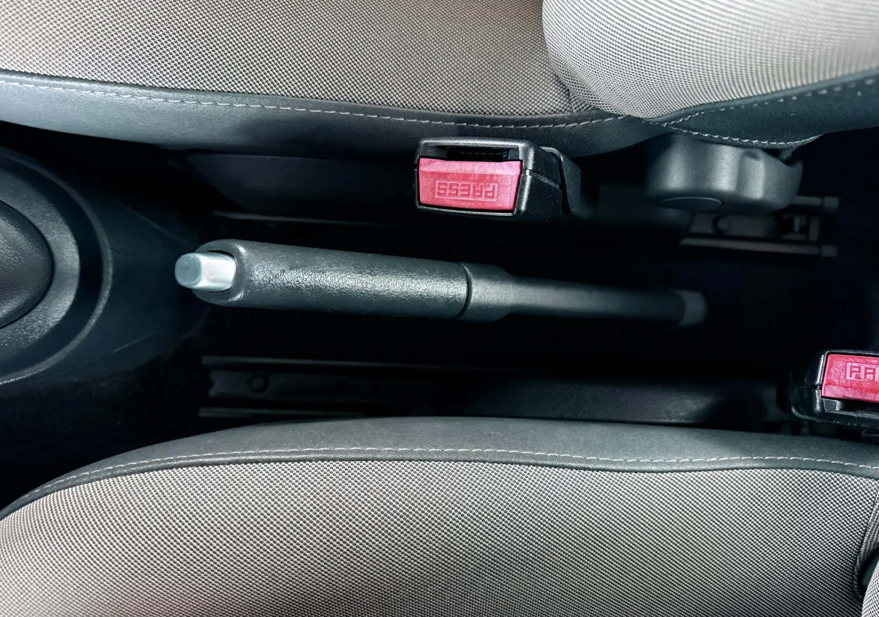 Vue rapprochée de la poignée de frein à main et des ceintures de sécurité grises à l'intérieur d'une Renault Twingo II.