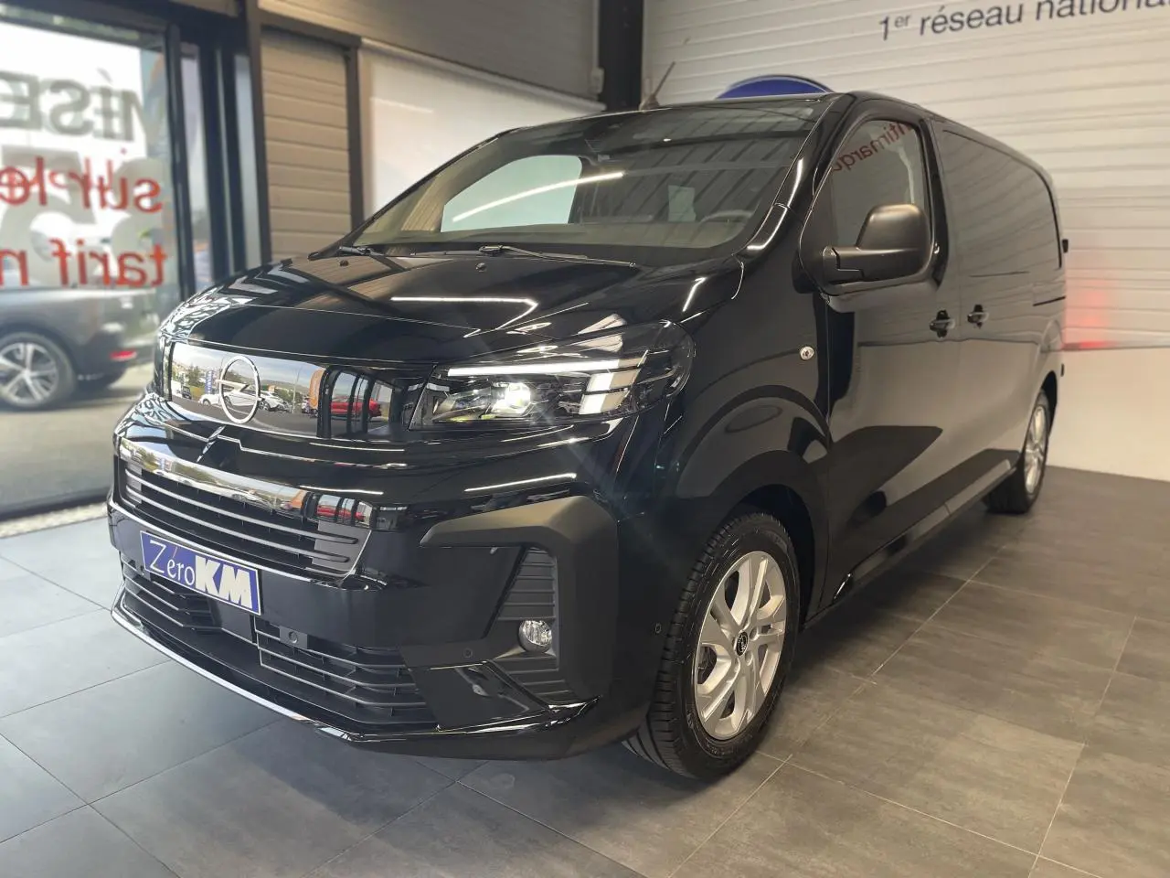 Vue 3/4 avant droit d'un Opel Vivaro noir carbone avec calandre chromée et phares allumés en showroom.