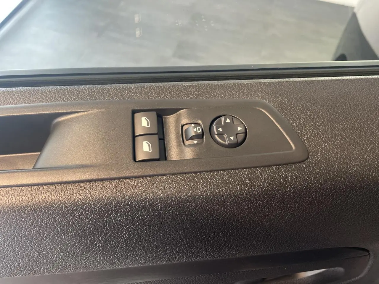 Gros plan sur les commandes de lève-vitres et réglage des rétroviseurs sur la porte côté conducteur d'un Opel Vivaro noir carbone.