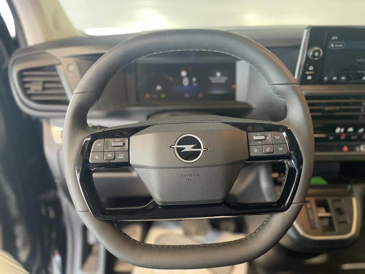 Gros plan sur le volant noir de l'Opel Vivaro 2025 avec commandes intégrées et tableau de bord numérique flou en arrière-plan.