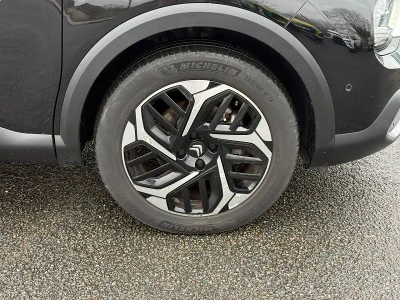 Gros plan sur la roue avant droite d'une Citroën C4 X 2024 noir Perla Nera avec jante alliage au design géométrique.