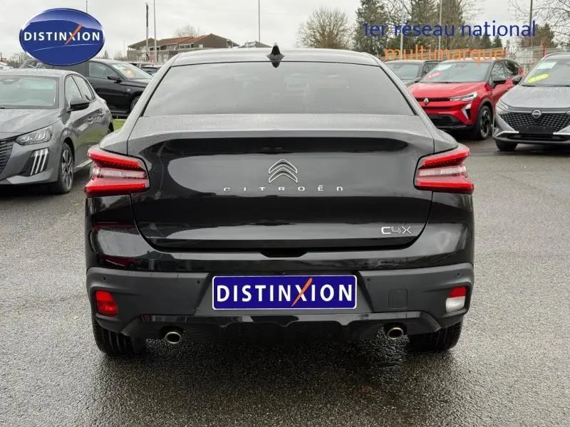 Vue arrière d'une Citroën C4 X 2024 noire Perla Nera avec feux LED et double sortie d'échappement visible sur parking.