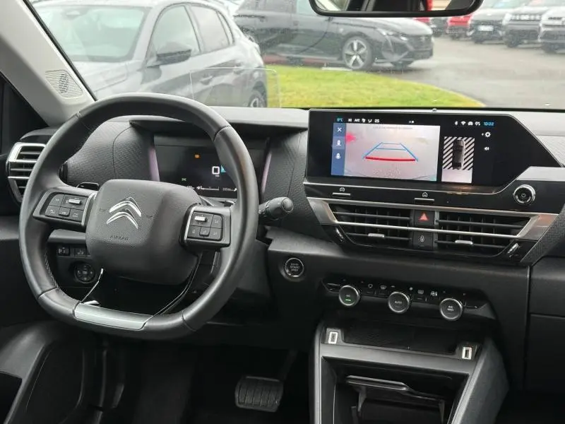 Vue intérieure du poste de conduite du Citroën C4 X 2024 noir, avec volant multifonction et écran tactile affichant la caméra de recul.