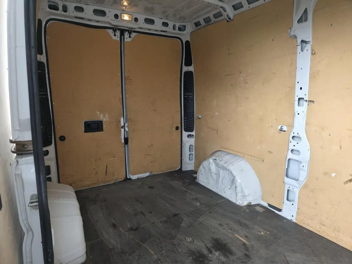 Vue intérieure arrière du fourgon blanc Opel Movano, montrant l'espace de chargement avec parois en bois et sol noir.