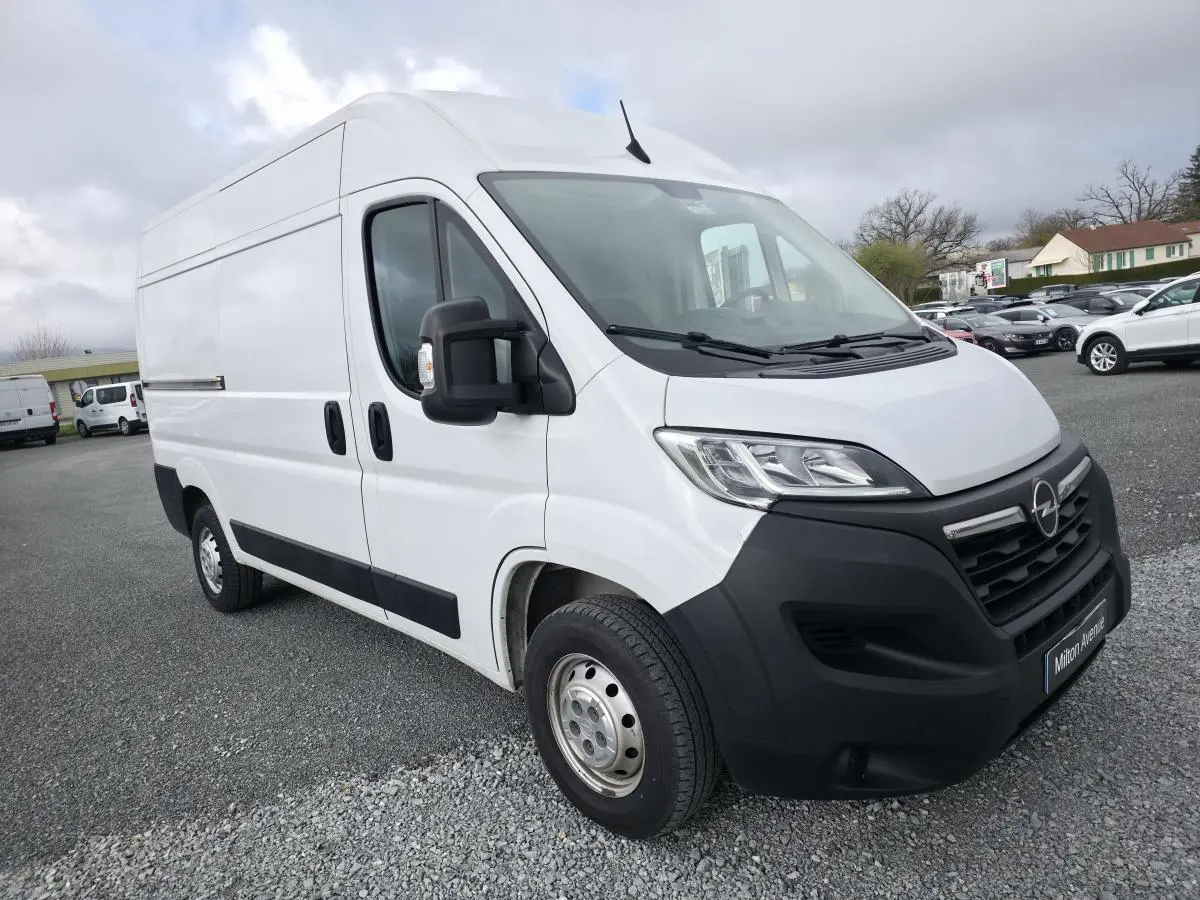 Vue 3/4 avant gauche d’un Opel Movano Fourgon blanc avec calandre noire et jantes tôles grises sur parking.