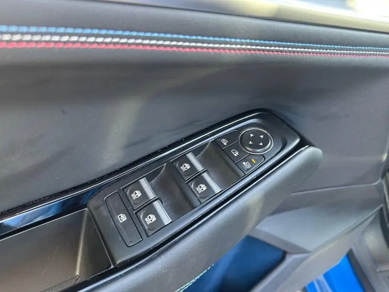 Gros plan sur la commande des vitres côté gauche avec surpiqûres bleues et rouges sur la porte du Renault Rafale bleu métallisé.