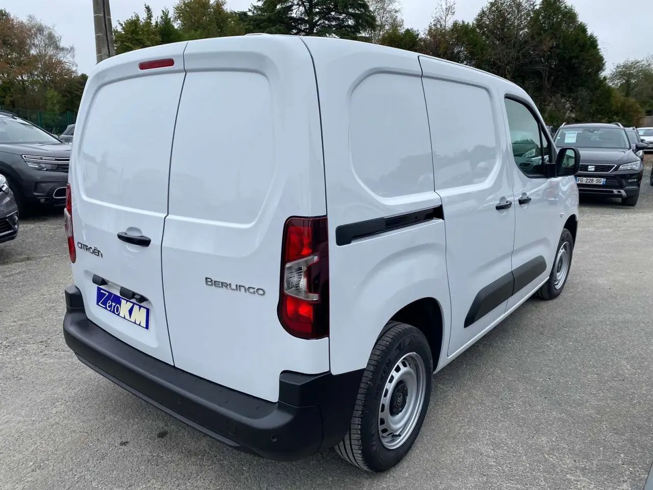 Vue 3/4 arrière droite d’un utilitaire Citroën Berlingo blanc avec protections latérales noires et porte arrière fermée.