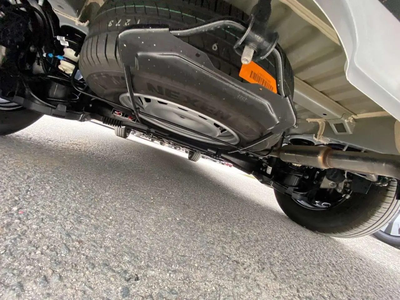 Vue sous le Citroën Berlingo blanc montrant la roue de secours suspendue sous le châssis et le système d'échappement.