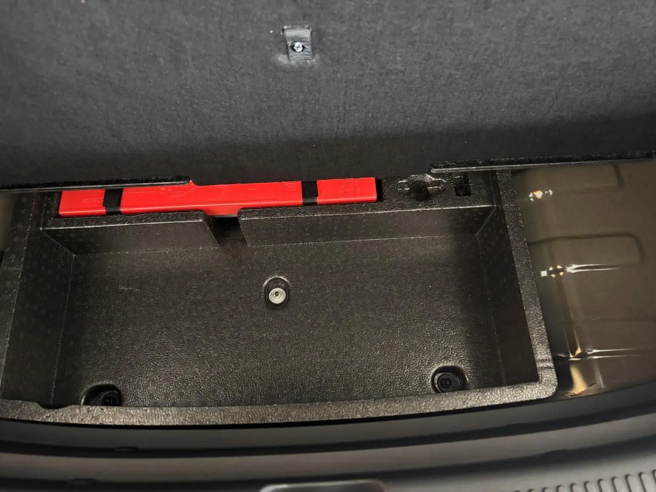 Coffre de rangement noir ouvert dans le coffre arrière du MG Motor ZS 1.5 Hybrid+ Luxury 2026, avec un triangle de signalisation rouge visible.