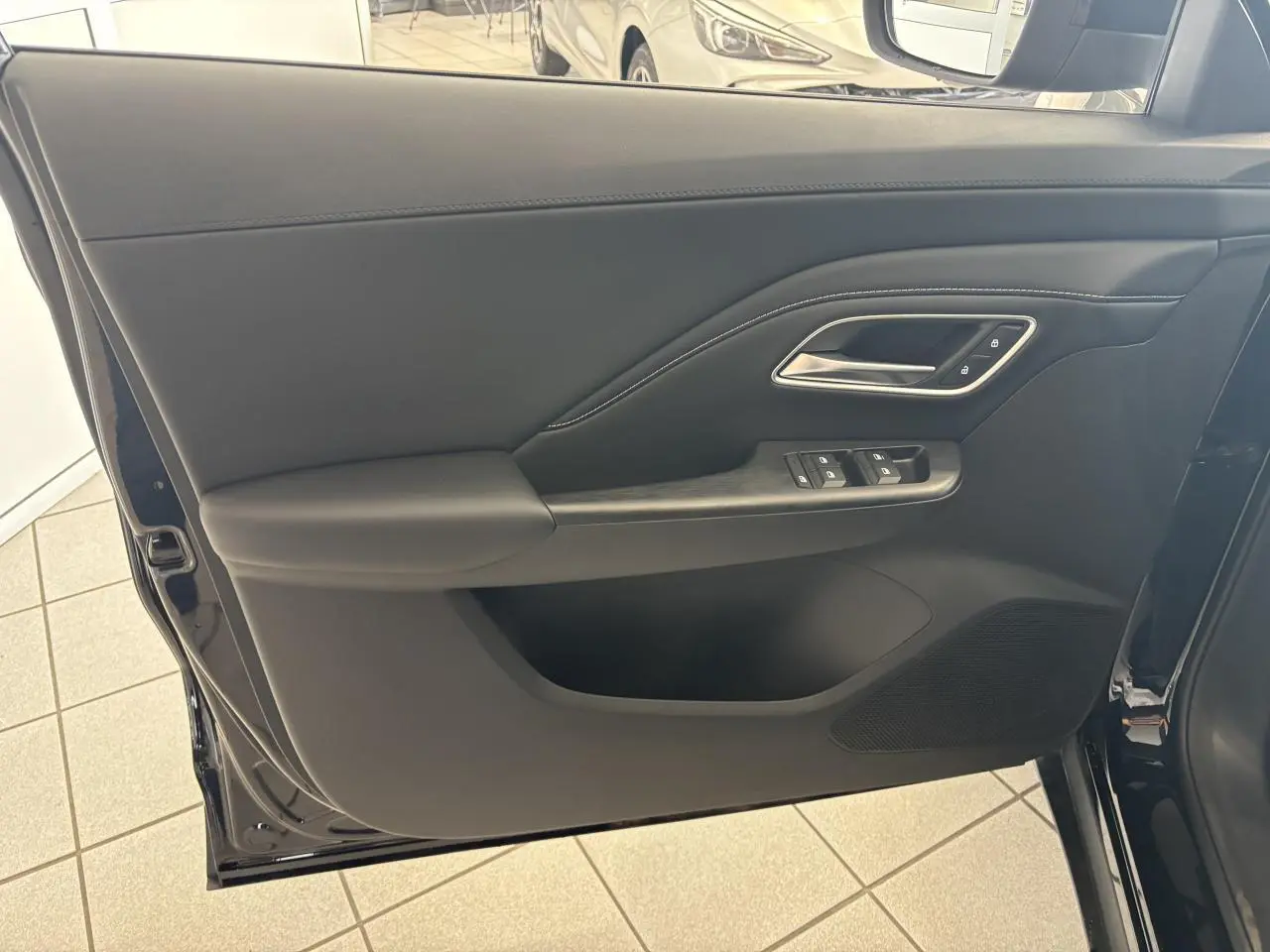 Porte avant gauche ouverte d’un MG MOTOR ZS 1.5 Hybrid+ noir, montrant les commandes de vitres et la poignée intérieure chromée.
