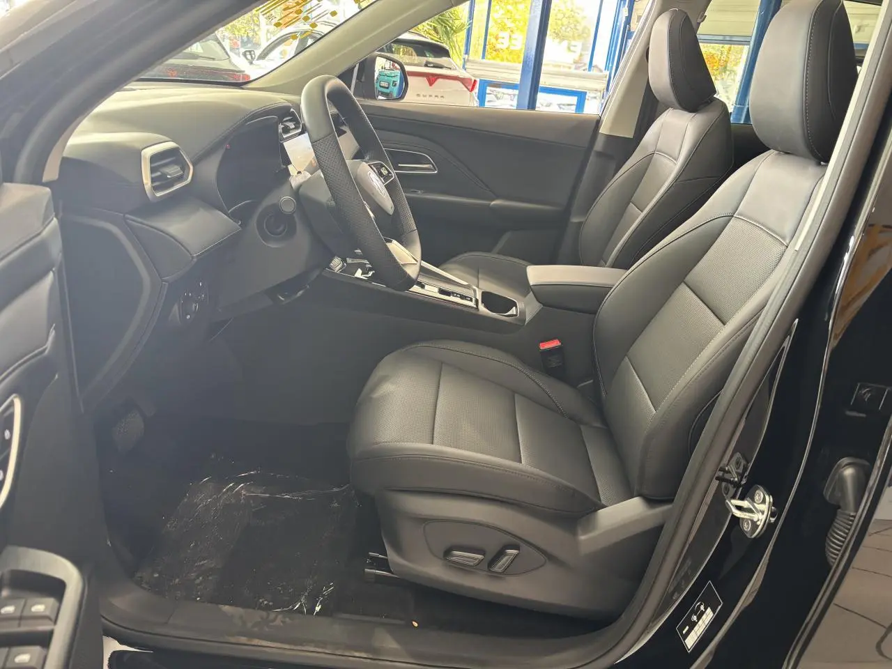 Vue intérieure côté conducteur du MG Motor ZS 1.5 Hybrid+ noir, sièges en tissu/similicuir noir et tableau de bord moderne.
