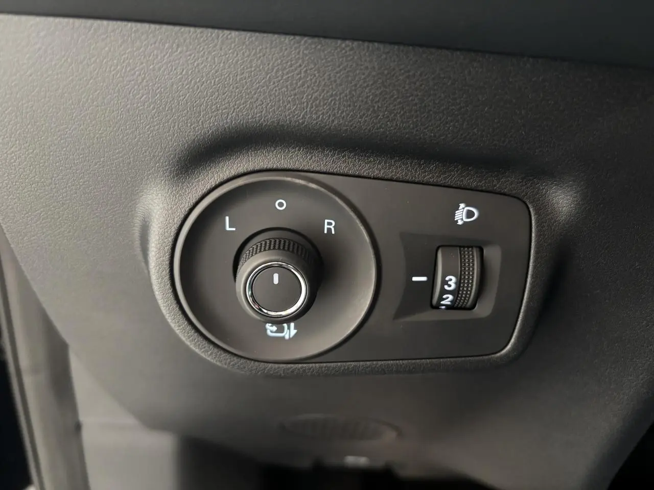 Gros plan sur les commandes de réglage des rétroviseurs et des phares du MG Motor ZS 1.5 Hybrid+ noir, côté conducteur.