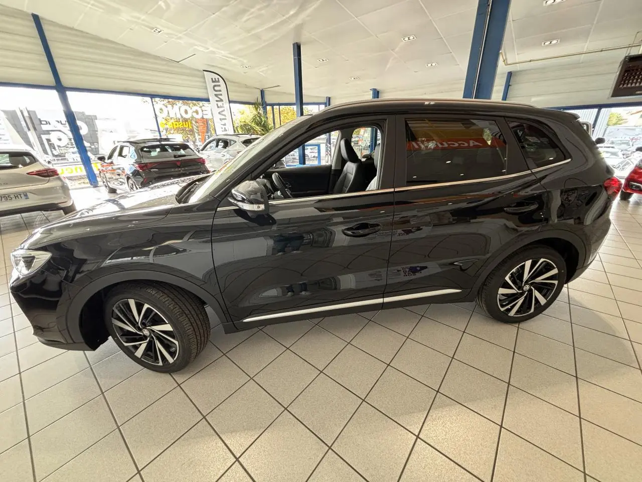 Vue de profil côté gauche du MG ZS 1.5 Hybrid+ noir, avec jantes alliage et intérieur visible en concession.
