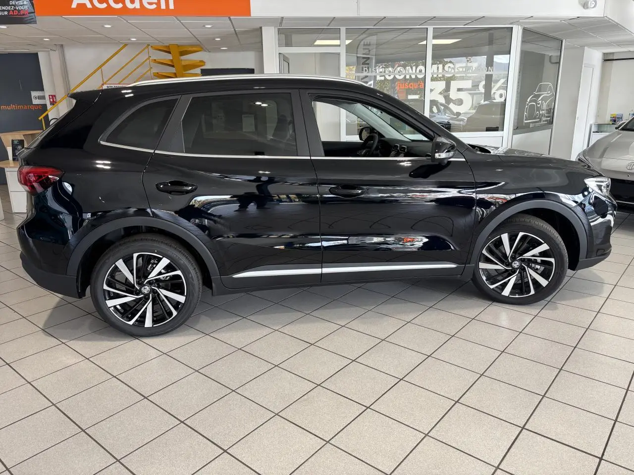 Vue de profil côté gauche du SUV MG ZS 1.5 Hybrid+ noir brillant, avec jantes alliage 18 pouces en concession.
