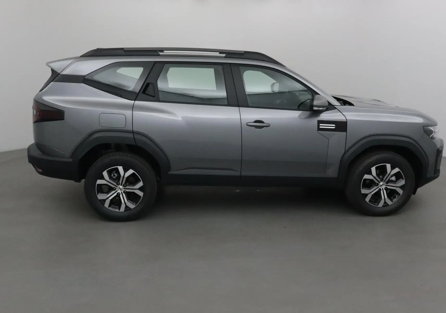 Profil côté droit du SUV Dacia Bigster gris schiste avec barres de toit et jantes alliage modernes.