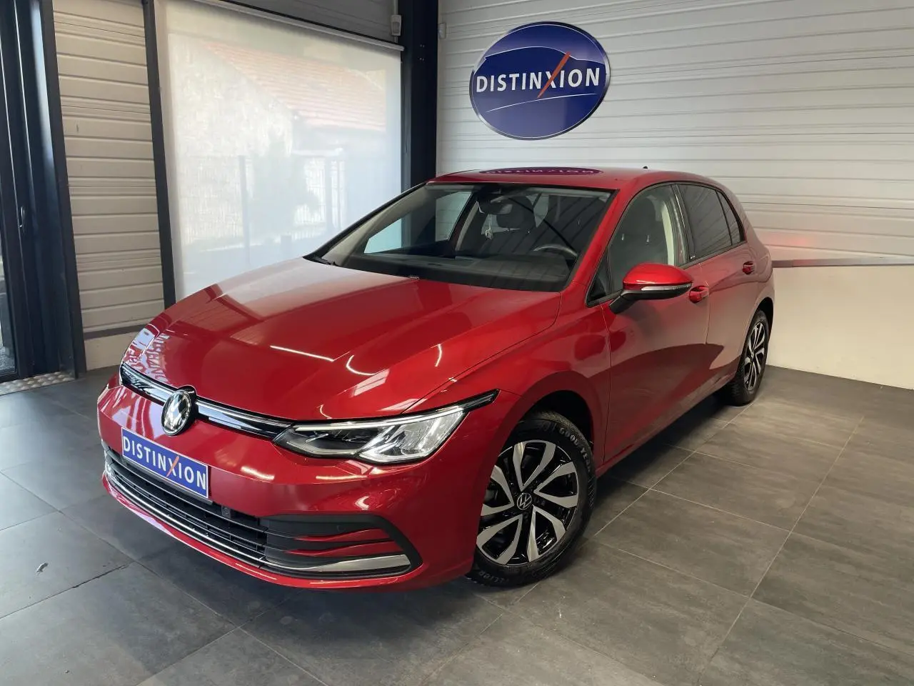 Vue 3/4 avant droite d'une Volkswagen Golf rouge métal avec jantes alliage et logo VW visible sur le capot.