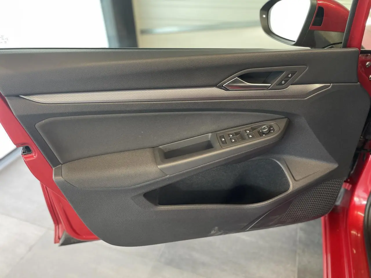 Porte avant gauche ouverte d'une Volkswagen Golf rouge métal 2022, montrant les commandes de vitres et la poignée intérieure chromée.