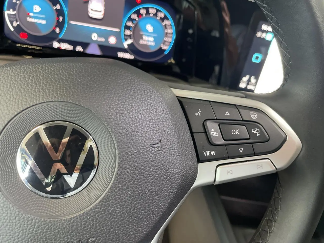 Gros plan sur le volant multifonction noir de la Volkswagen Golf 8 avec tableau de bord digital en arrière-plan.