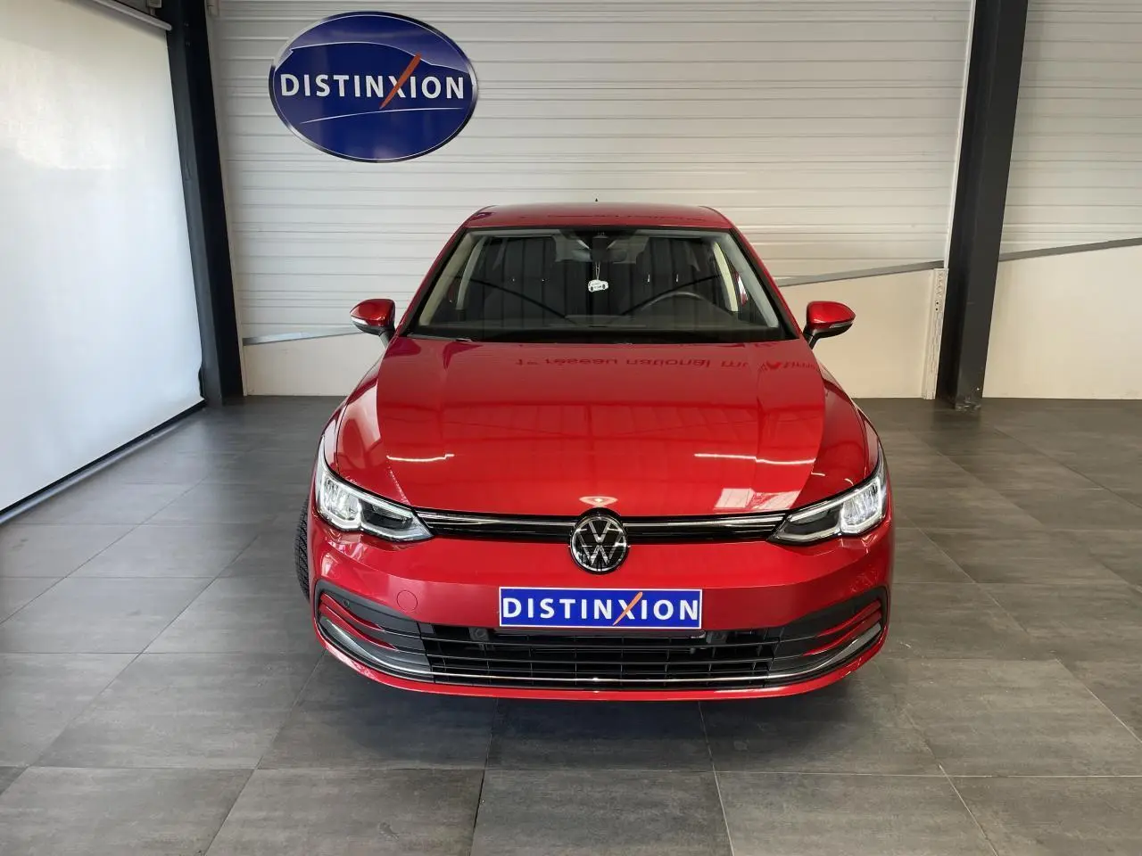 Volkswagen Golf 8 Active rouge métal vue de face en intérieur avec logo Distinxion visible.