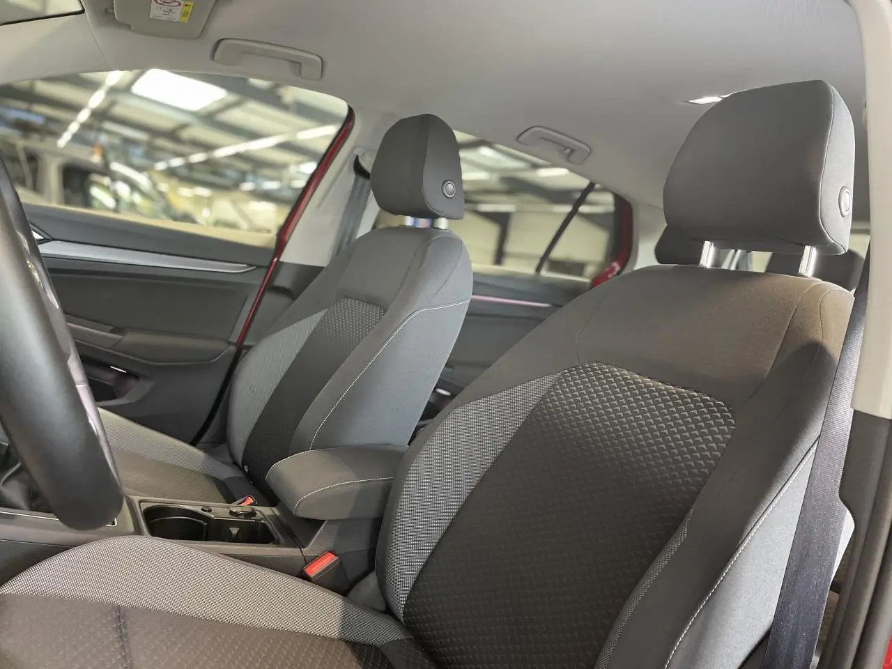 Intérieur avant de la Volkswagen Golf rouge métal 2022, sièges tissu Waveform gris et noir avec accoudoir central.