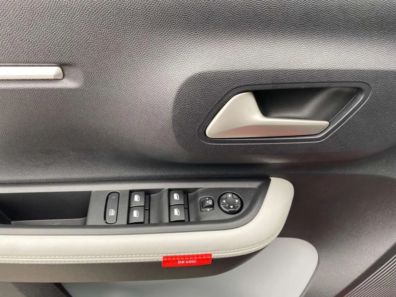 Gros plan sur la poignée intérieure et les commandes des vitres côté conducteur de la Citroën C3 rouge Elixir toit noir.