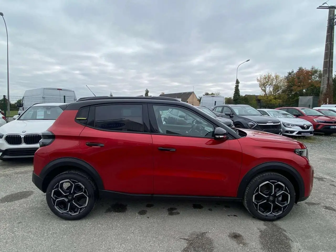 Profil côté gauche d'une Citroën C3 2025 rouge Elixir avec toit noir et jantes alliage 17 pouces sur parking.