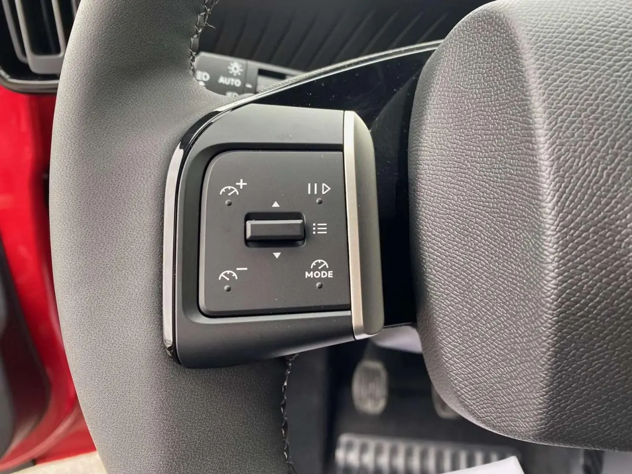 Détail du bouton de commande du régulateur de vitesse sur le volant d'une Citroën C3 rouge Elixir avec toit noir.