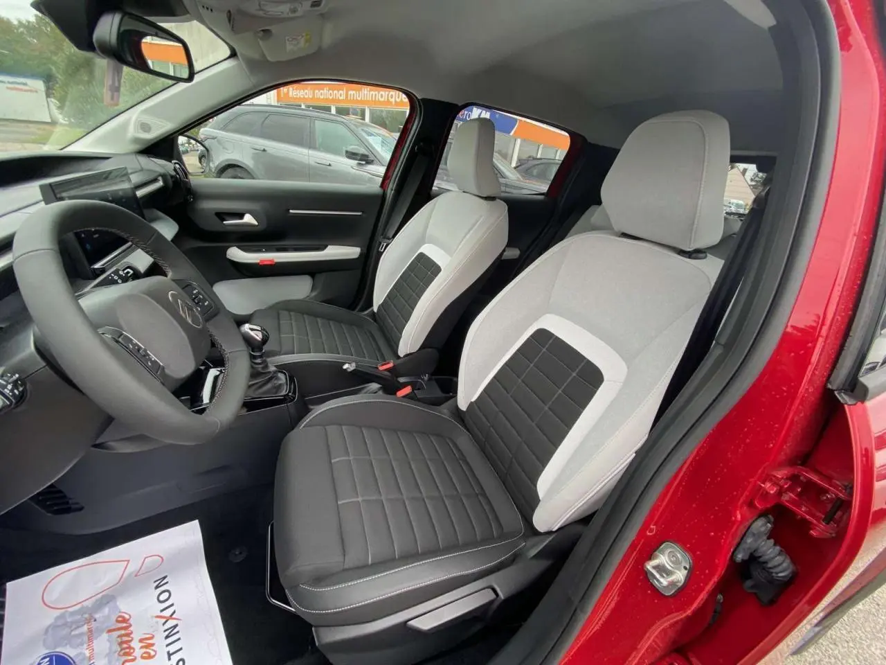 Intérieur avant de la Citroën C3 rouge Elixir, sièges bicolores gris et noir, volant et tableau de bord visibles.