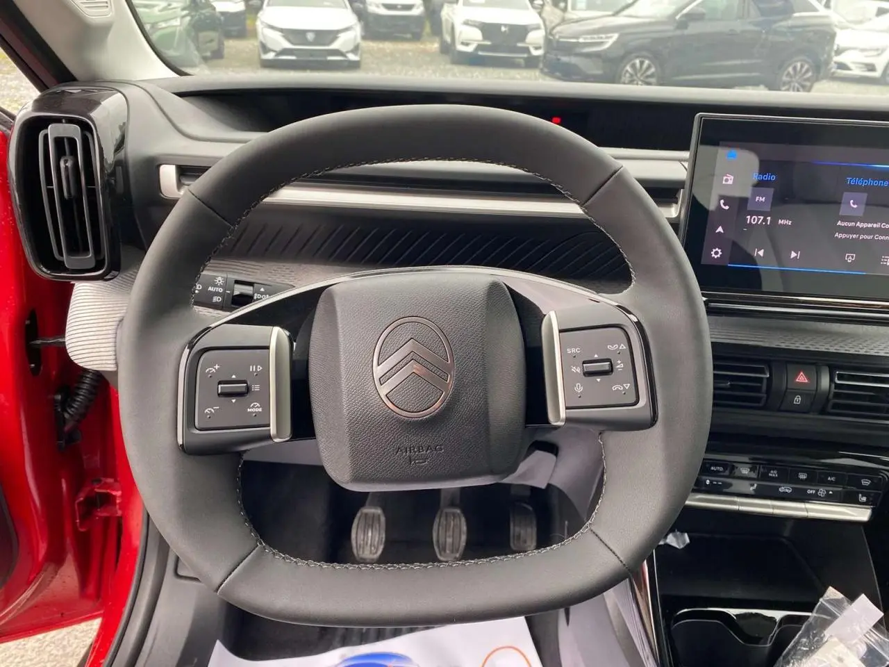 Vue intérieure centrée sur le volant carré du Citroën C3 rouge Elixir avec tableau de bord et écran tactile visible.