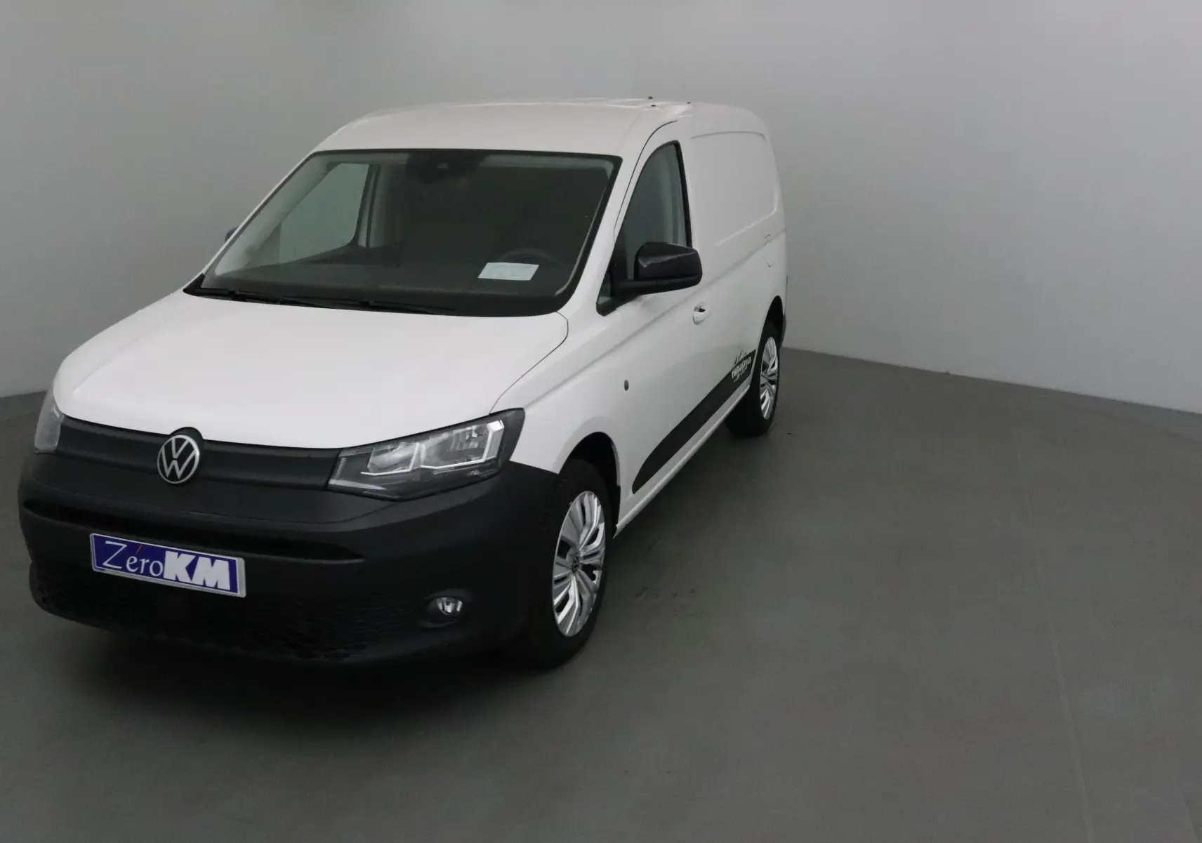 Vue 3/4 avant d'un Volkswagen Caddy Maxi blanc avec bouclier noir et logo VW bien visible.