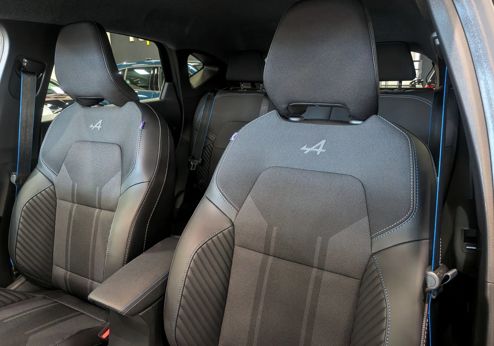 Gros plan sur les sièges avant noirs avec surpiqûres bleues et logo Alpine du Renault Captur E-TECH 2025.