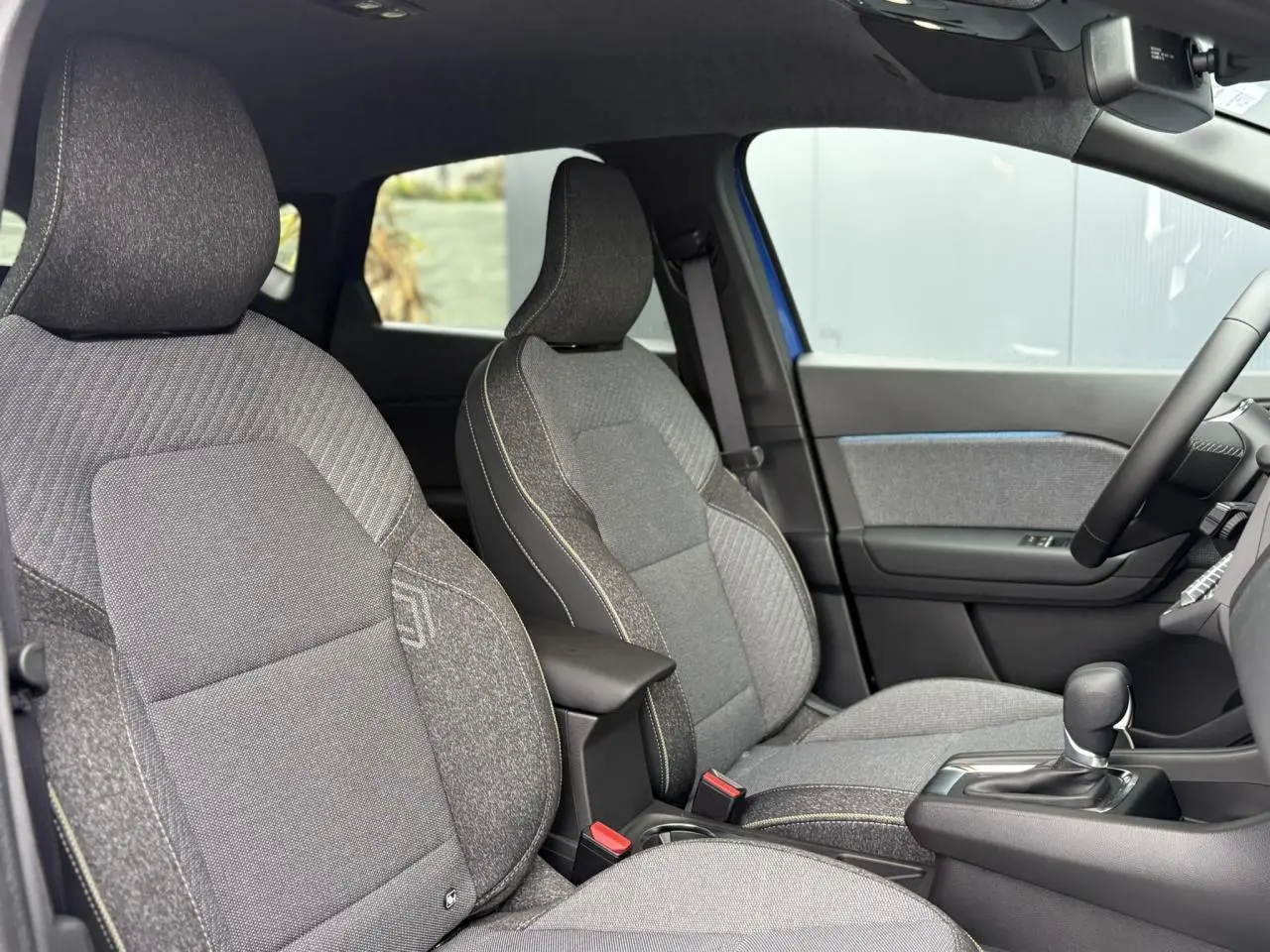 Vue intérieure côté conducteur du Renault Captur 2025, sièges gris texturés avec console centrale et volant textile.