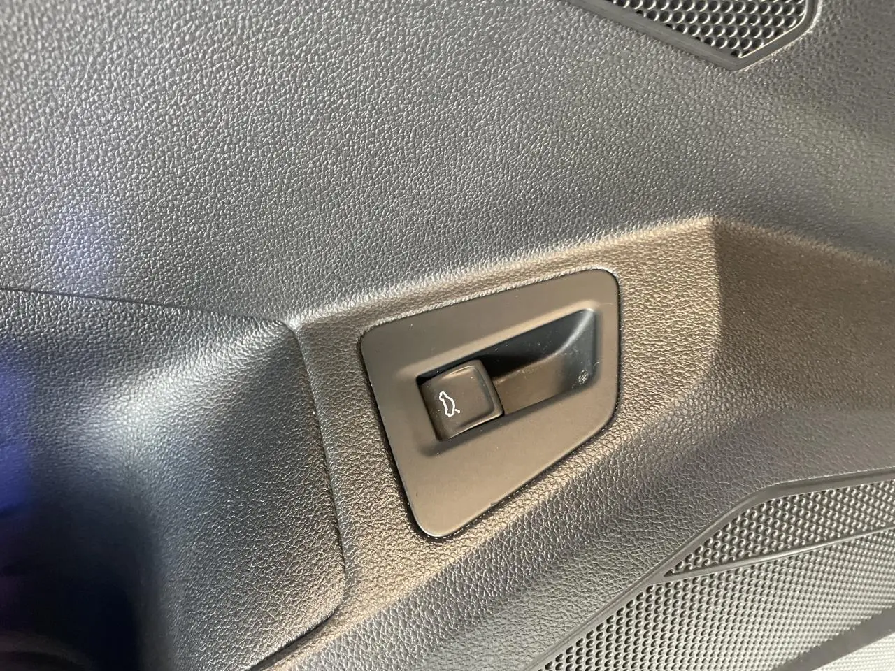 Gros plan sur le bouton d'ouverture électrique du hayon dans l'habitacle noir du Volkswagen Touareg blanc.