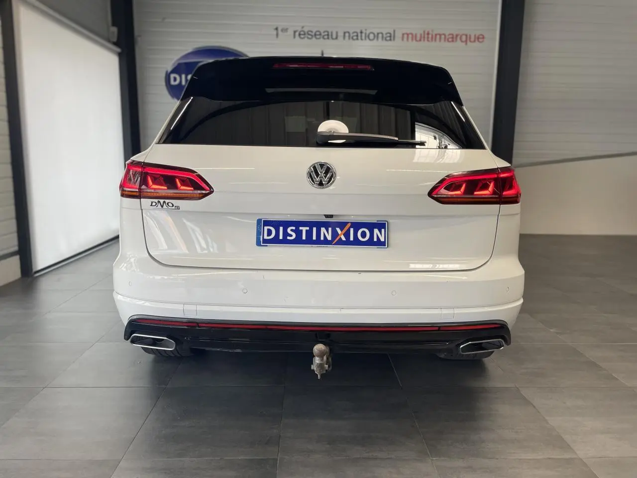 Vue arrière d'un Volkswagen Touareg blanc avec feux LED, double sortie d'échappement et attelage visible en intérieur showroom.
