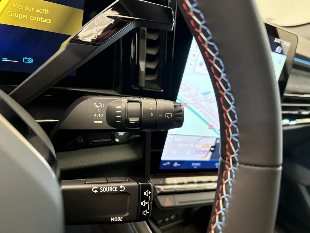 Gros plan intérieur sur le volant avec surpiqûres tricolores et commande multifonctions, écran tactile de navigation visible.