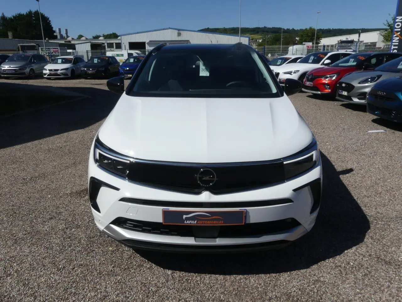 Vue avant d'un Opel Grandland blanc métallisé avec calandre noire brillante et phares LED, sur un parking extérieur.
