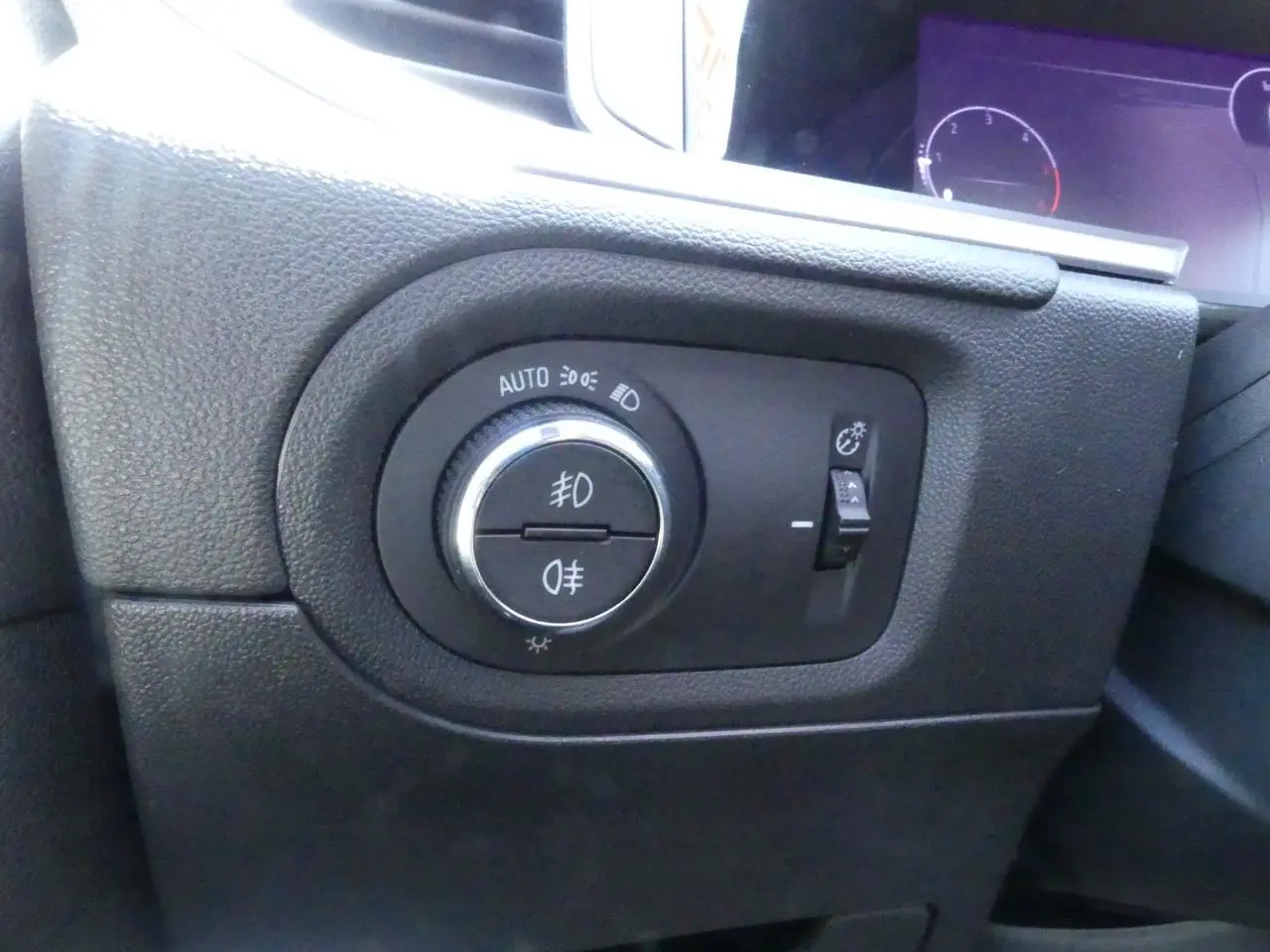 Gros plan sur le bouton de commande des phares et feux antibrouillard à gauche du tableau de bord de l'Opel Grandland 2024.