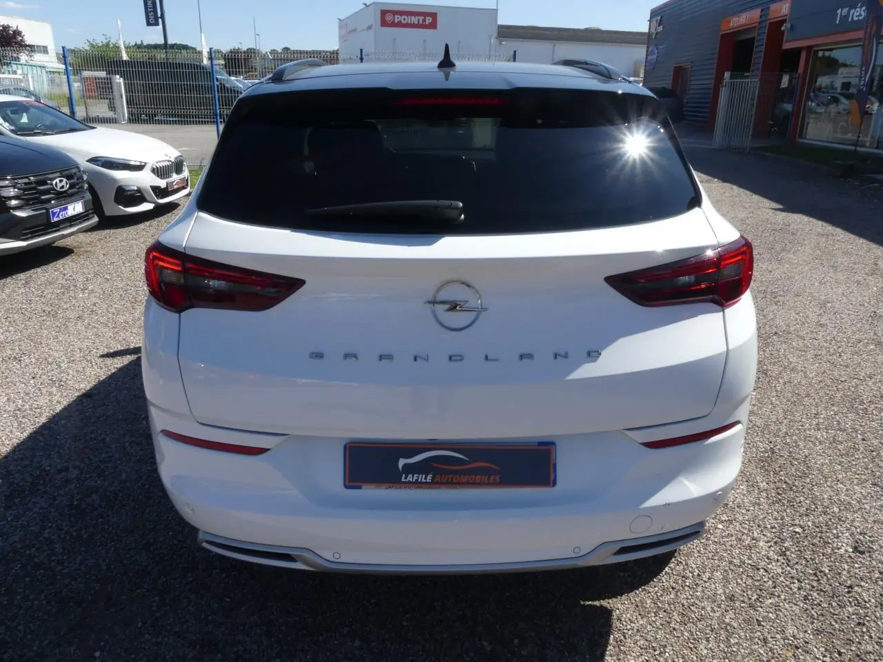 Vue arrière d'un Opel Grandland blanc métallisé avec vitres arrière surteintées et feux LED, en extérieur sur parking.